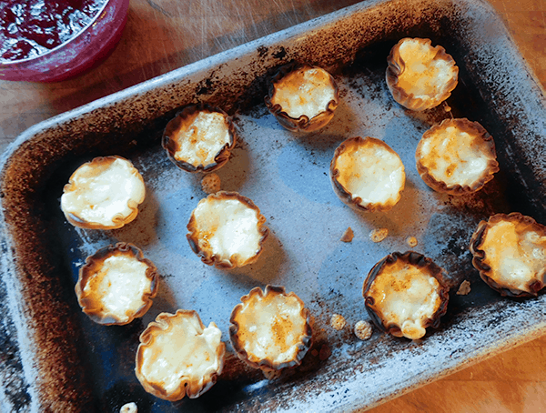 Phyllo cups with melted cheese on a baking sheet