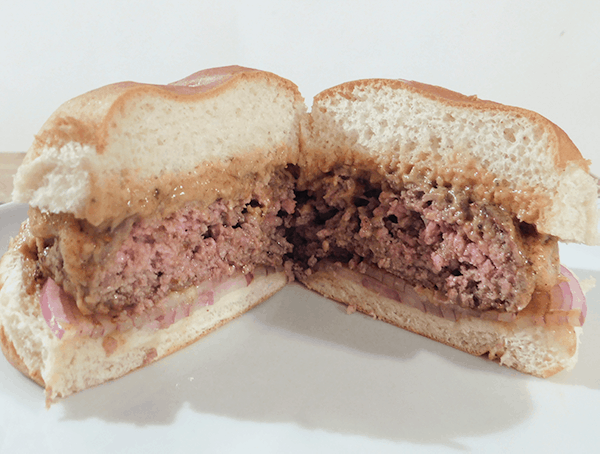 Side view of a cooked burger on a bun with Peanut Sauce