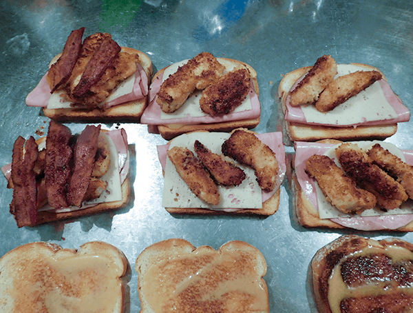 Toast on a silver surface with bacon, cheese, ham and chicken