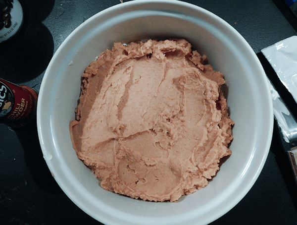 Refried Beans in a casserole dish making Six Layer Corn Dip