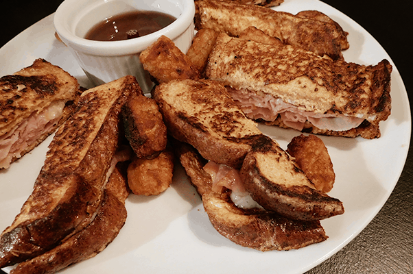 White plate of ham and cheese stuffed French toast and tater tots