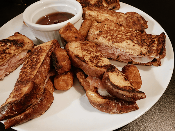 White plate of ham and cheese stuffed French toast and tater tots